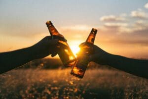 Two beers clinking together in front of a sunset.